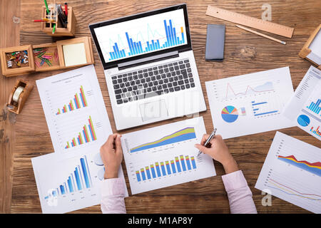 Imprenditrice analizzare diverse grafico posto sulla scrivania Foto Stock