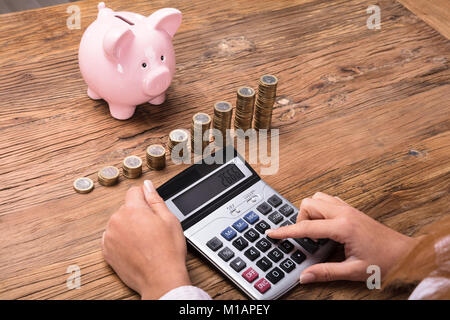 Donna finanze di calcolo utilizzando la Calcolatrice sulla scrivania in legno Foto Stock