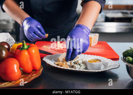 Ritagliato colpo di chef mettendo le fette di formaggio sulla piastra Foto Stock