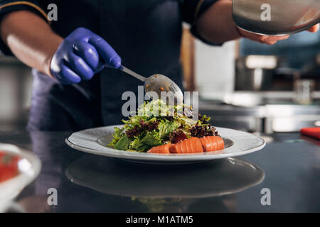 Ritagliato colpo di chef salsa di colata su insalata dal cucchiaio Foto Stock