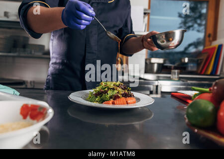 Ritagliato colpo di chef salsa di colata su insalata Foto Stock