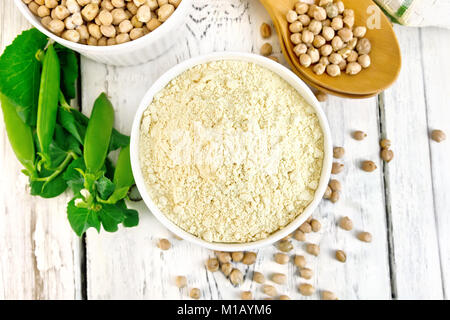 La farina di ceci e cece in bianco ciotole e cucchiai, baccelli di fagioli verdi, un centrino sullo sfondo dei pannelli in legno sulla parte superiore Foto Stock