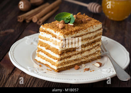 Fetta di più livelli di torta di miele russo Medovik decorate con la menta e le mandorle sulla piastra bianca Foto Stock