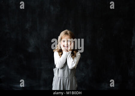 Pretty girl sorge sullo sfondo nero di una lavagna e sorriso. sfondo con uno spazio libero Foto Stock