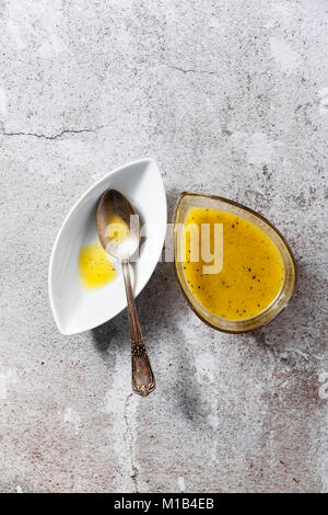 Condimento per insalata da olio di oliva e limone in un piatto di portata e un cucchiaio d'argento su un tavolo di pietra Foto Stock