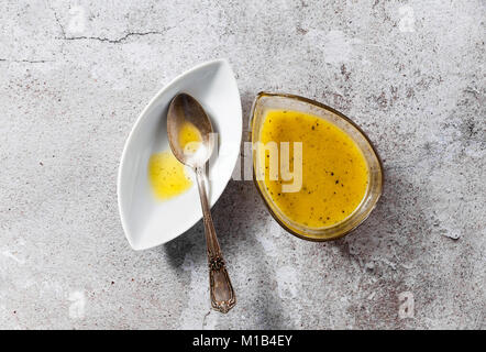 Condimento per insalata da olio di oliva e limone in un piatto di portata e un cucchiaio d'argento su un tavolo di pietra Foto Stock