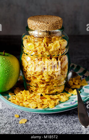 Cornflake di cereali in un barattolo di vetro per la conservazione di latte e una mela verde , colazione veloce Foto Stock