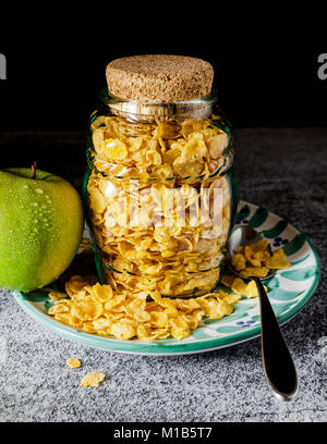 Cornflake di cereali in un barattolo di vetro per la conservazione di latte e una mela verde , colazione veloce Foto Stock