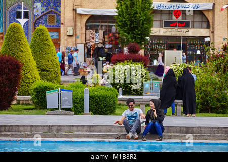 Isfahan, Iran - 24 Aprile 2017: una giovane coppia iraniano è seduto vicino a una moschea di fronte a una fontana su una data e allegramente la chat, il Naqsh-e JAHAN Foto Stock