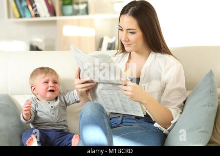 Il pianto del bambino esigente di attenzione e di sua madre ignorando lui seduto su un divano nel salotto di casa Foto Stock