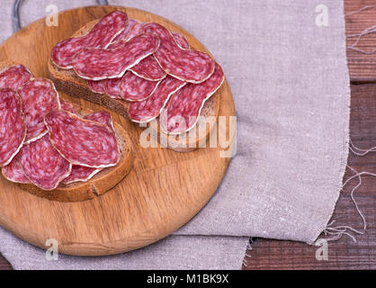 Pezzi di salsiccia affumicata salame sul pane di segale, panini giacciono su una cucina in legno board Foto Stock