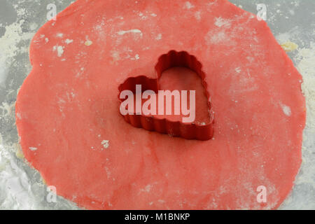 Cuore cookie cutter e zucchero rosso pasta biscotto su un foglio di alluminio con la farina per rendere il giorno di San Valentino i cookie Foto Stock