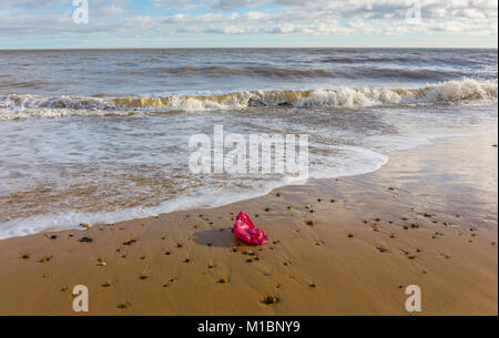 In rosso di un sacchetto di plastica - lettiera/inquinamento sulla riva del mare. Il mare del Nord a Southwold, Suffolk.