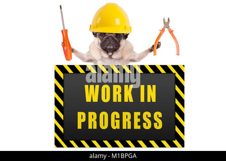 Pug dog indossando costruttore giallo casco di sicurezza, tenendo in mano una pinza e un cacciavite con il cartello di avviso dicendo work in progress, isolato su bianco backgrou Foto Stock