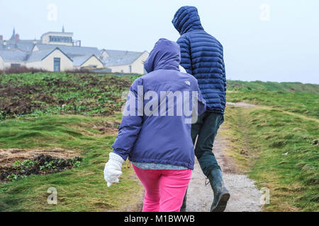 Regno Unito Inverno Meteo - due persone walkers difficoltà a camminare contro vento alta sulla costa di Newquay Cornwall. Foto Stock