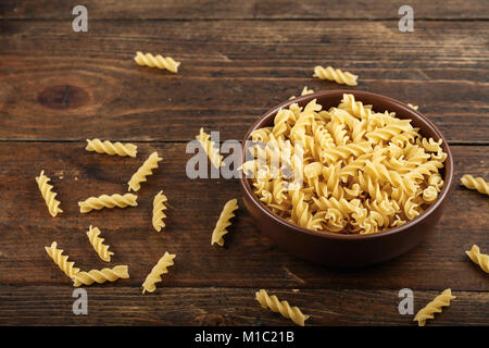 La pasta grezza in una piastra su un legno marrone sfondo, accanto ad un piatto di pasta diffusa Foto Stock