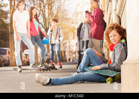 Vista laterale ritratto di ragazzo adolescente seduta sul marciapiede con lo skateboard e ascolto di musica Foto Stock