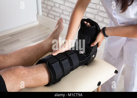 Close-up di un ortopedico mettendo a piedi il rinforzo alla gamba del paziente Foto Stock