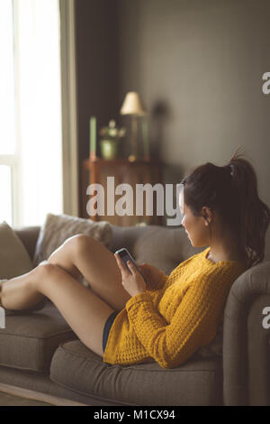 Donna che utilizza un cellulare in salotto Foto Stock