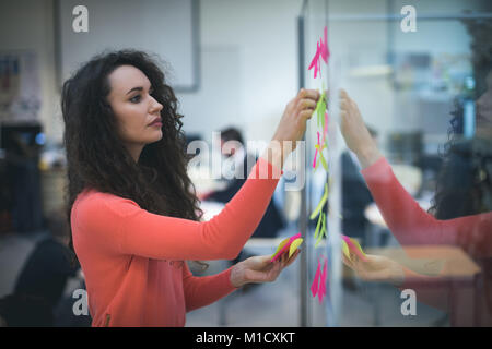 Femmina incollaggio executive note adesive sulla parete di vetro Foto Stock