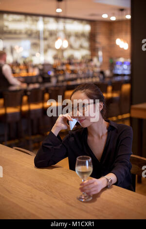 Donna che parla su mobile pone pur avendo il vino Foto Stock