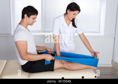 Terapista del sesso femminile assistere paziente di sesso maschile mentre si estende la sua gamba in ospedale Foto Stock