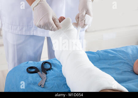 Close-up di un medico della mano bendaggio di legatura sulla persona il piede in clinica Foto Stock