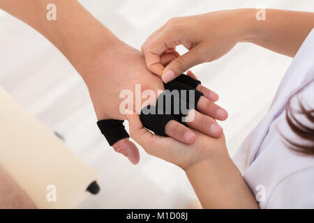 Elevato angolo di visione di un medico mettendo il dito la protezione per manicotto sull'uomo del dito in clinica Foto Stock