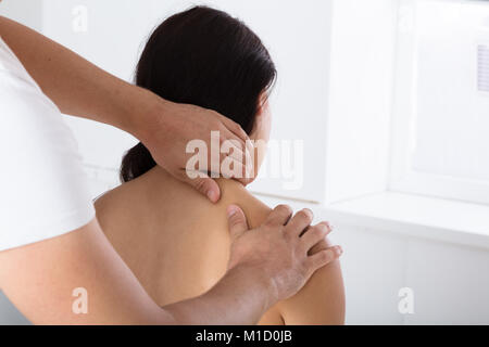 Vista posteriore di una giovane donna ricevere massaggio della spalla dal massaggiatore Foto Stock