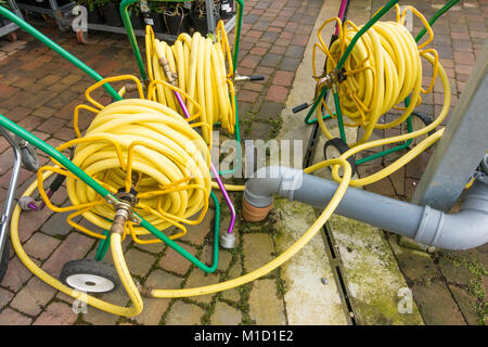 Tre mercati giardino avvolgitubo con giallo attorcigliare il tubo flessibile resistente su bobine portatile ed avente ugelli di spruzzo distribuzione conveniente in un garden center Foto Stock