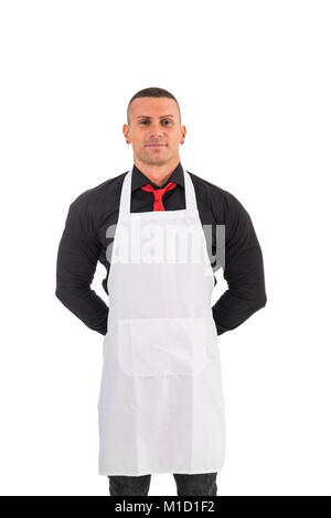 Il giovane chef o il cameriere in posa, accoglie gli ospiti con un sorriso, indossare un grembiule nero e camicia bianca isolata su sfondo bianco Foto Stock