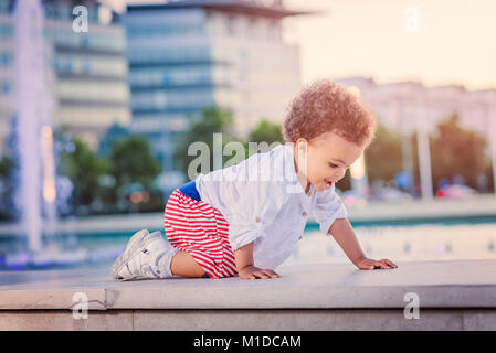 Carino bambina giocando accanto alla fontana di sprinkler Foto Stock