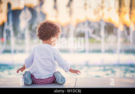 Carino bambina giocando accanto alla fontana di sprinkler Foto Stock