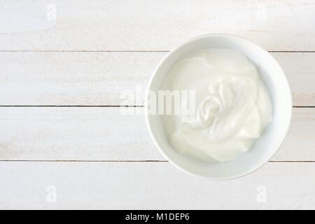 Lo yogurt greco in una ciotola bianca, vista sopra un bianco sullo sfondo di legno Foto Stock