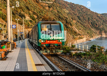 Un treno viaggia in Monterosso al Mare stazione ferroviaria sulla costa di Cinque Terre d'Italia come viaggiatori sedersi e godere di una calda giornata di inizio autunno Foto Stock