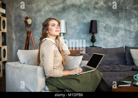 I giovani designer donna seduta a casa scrivania in ufficio con il computer portatile. Attraente modello allegro tramite computer. Ragazza che lavora in studio. Vera donna fumetto di lavoro Foto Stock