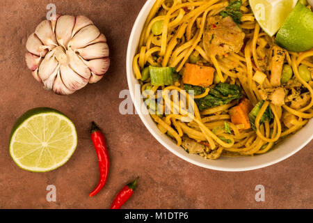 Giallo in stile Tailandese pollo al curry con pasta e patate dolci contro uno sfondo rosso Foto Stock