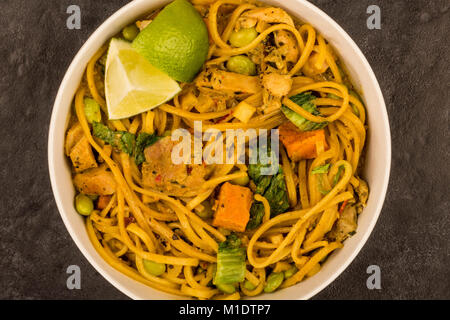 Giallo in stile Tailandese pollo al curry con pasta e patate dolci contro uno sfondo nero Foto Stock