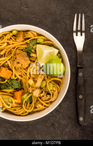 Giallo in stile Tailandese pollo al curry con pasta e patate dolci contro uno sfondo nero Foto Stock