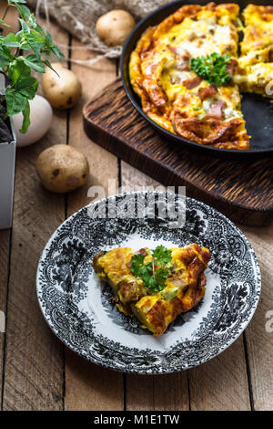 Un pezzo di francese omelette cotte savoiardo con prosciutto e formaggio, patate e porri su una piastra, in stile rustico, vista dall'alto Foto Stock