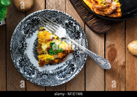 Frittata con pancetta, patate, porri e formaggio su una piastra, vista dall'alto Foto Stock