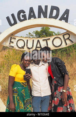Giovani adulti ugandesi facendo una foto selfie al marcatore per l'equatore in Uganda. Foto Stock