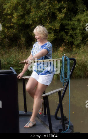 Donna che utilizza il timone per sterzare una narrowboat lungo un canale in inglese Foto Stock