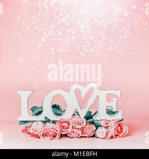 La parola amore pastello su sfondo rosa con un bellissimo mazzo di rose e bokeh , vista frontale. Creative vacanze femmina formato con spazio di copia per il messaggio di saluto Foto Stock
