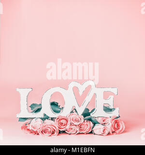 La parola amore pastello su sfondo rosa con un bellissimo mazzo di rose, vista frontale. Creative vacanze femmina formato con spazio di copia per il messaggio di saluto Foto Stock
