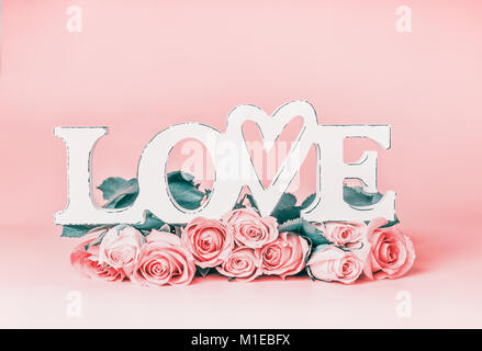 La parola amore pastello su sfondo rosa con rose mazzetto, vista frontale. Creative vacanze femmina formato con spazio di copia per il messaggio di saluto Foto Stock