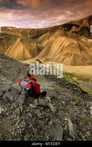 L'Islanda. Landmannalaugar Parco Nazionale. Tourist, escursionista donna in appoggio sulla collina rocciosa, godendo della vista. Foto Stock