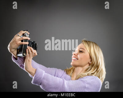 Attraente giovane donna in rosa pallido con maglione vintage telecamera portatile su neutrale sfondo scuro, lo spazio per il testo Foto Stock