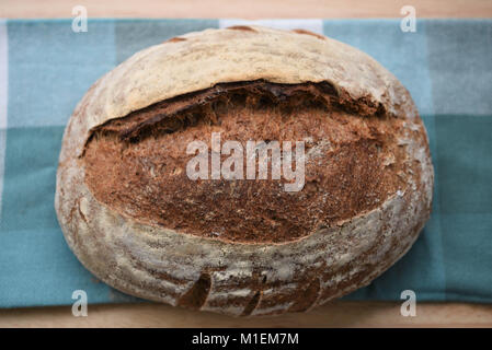 Alimentare artigianale di una fresca e fatta in casa focaccia cotta al forno del pane di pasta acida su un panno verde e pannello di legno o di tabella per una immagine rustico con vista aerea Foto Stock