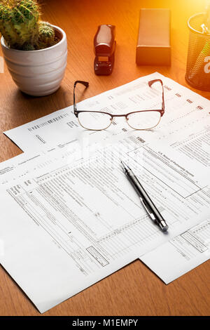 Noi moduli fiscali sul tavolo con gli occhiali, penna e cactus. Utile come noi moduli fiscali sfondo Foto Stock